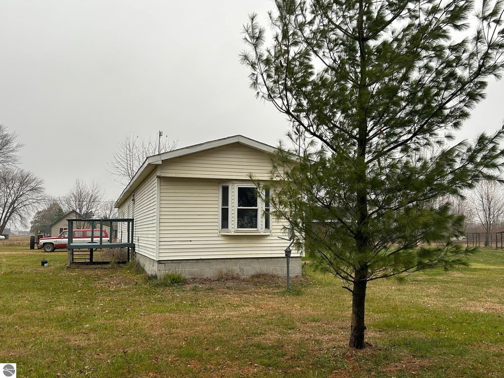 Single-story residential home with updated exterior, surrounded by grass and trees, featuring a small deck and visible utility pole, located on 1.87 acres in St Louis, MI.
