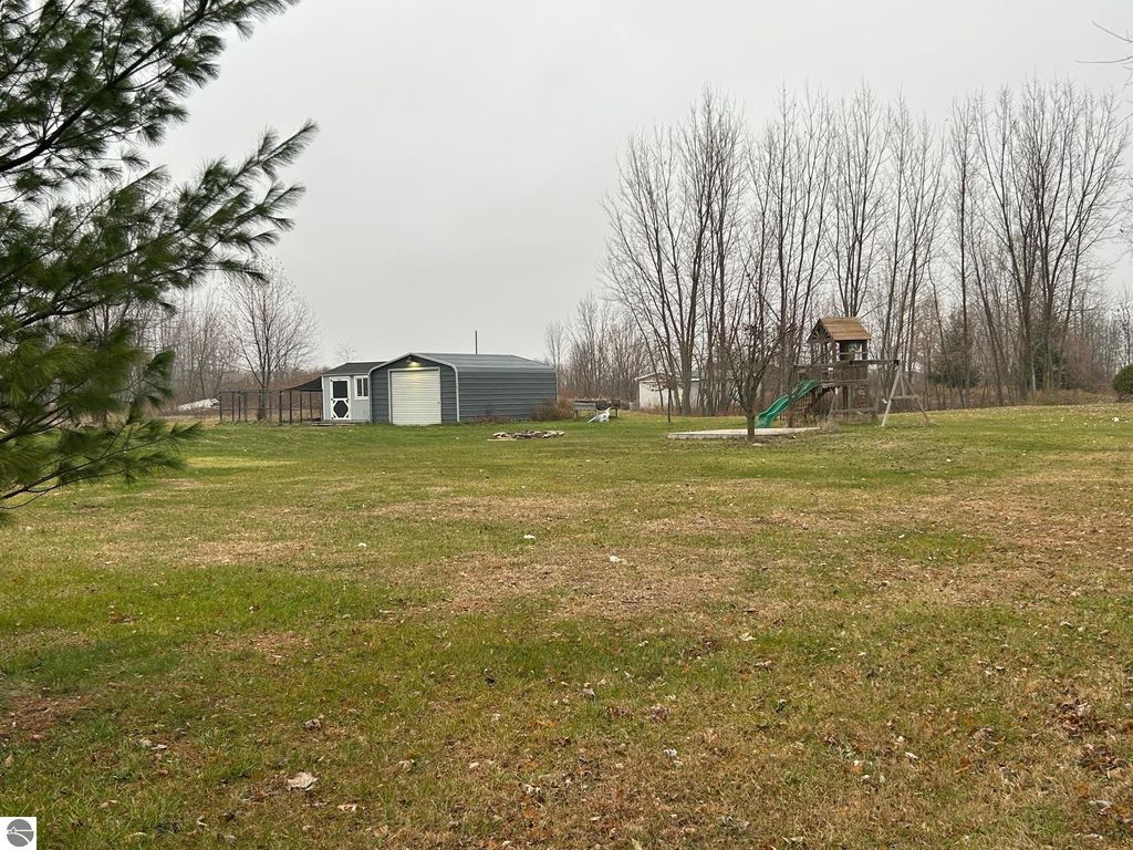 Spacious green yard at 3780 E North County Line Road, featuring a gray outbuilding, children's play structure with slide, and surrounding trees, ideal for country living.