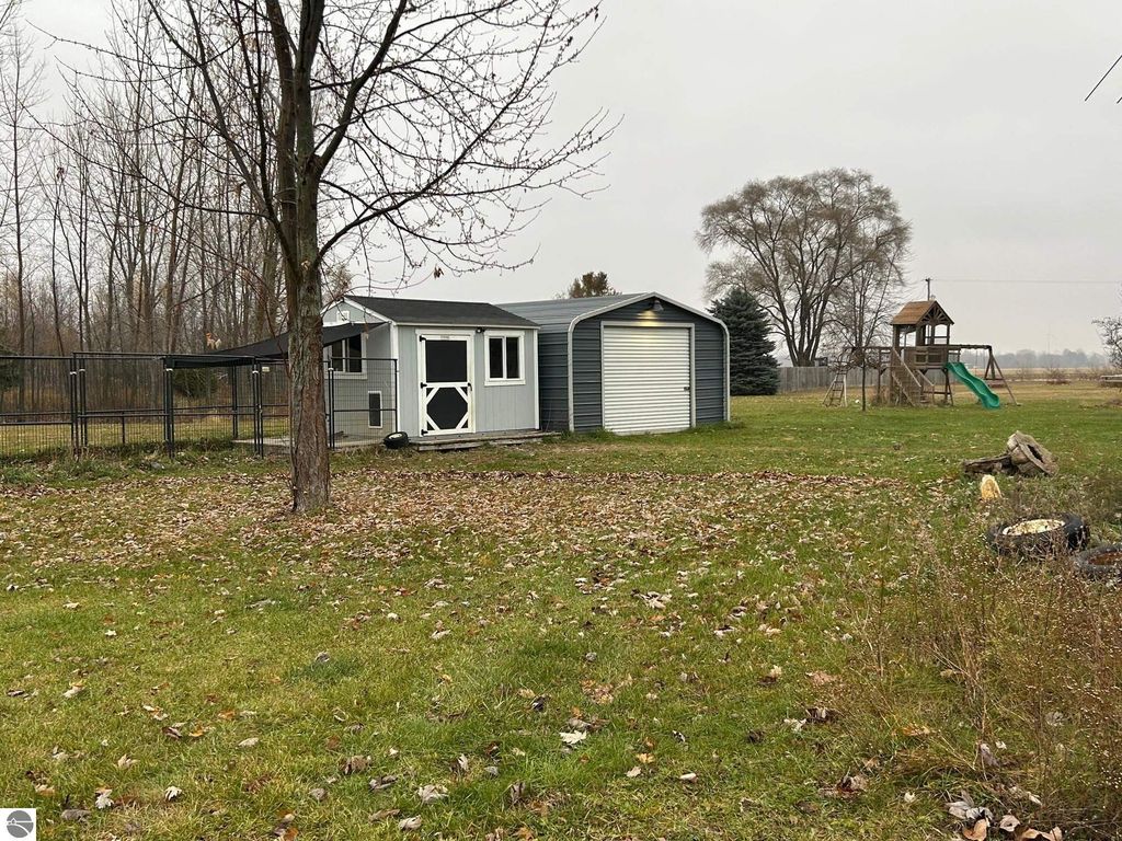 Heated garage and steel outbuilding on grassy lot with play structure and seasonal pond, showcasing country living at 3780 E North County Line Road, St Louis, MI.