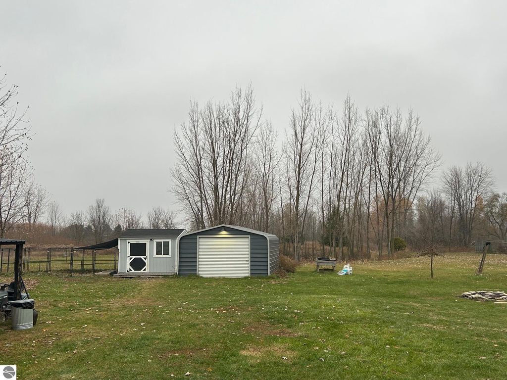 Outbuildings including a shed and a steel garage on a spacious grassy yard surrounded by trees, showcasing the country living aspect of the property at 3780 E North County Line Road, St Louis, MI.