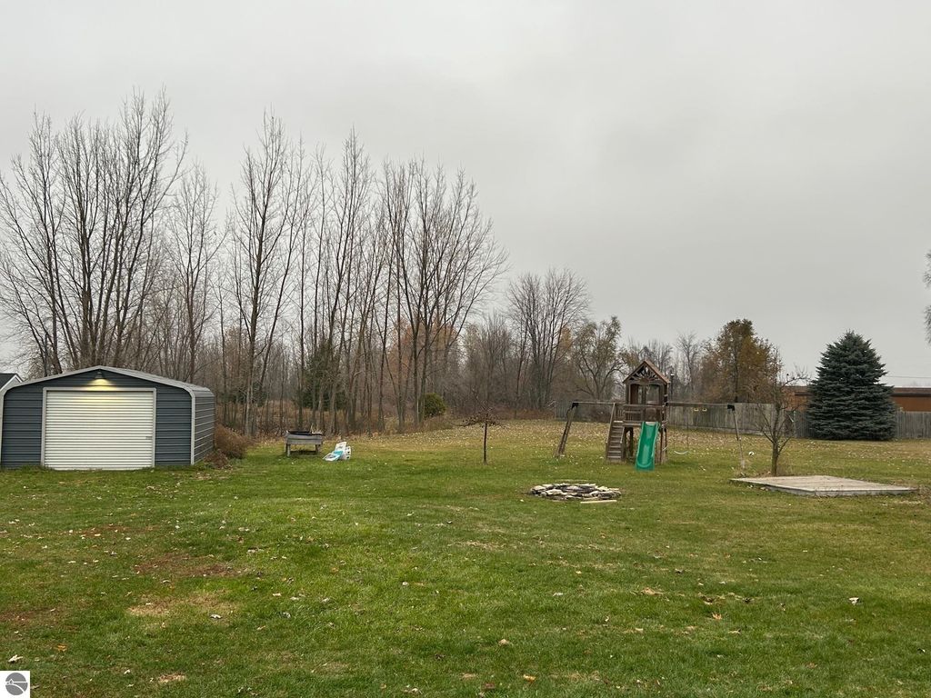 Country living with spacious yard featuring a steel outbuilding, play structure, and seasonal pond, surrounded by trees at 3780 E North County Line Road, St Louis, MI.