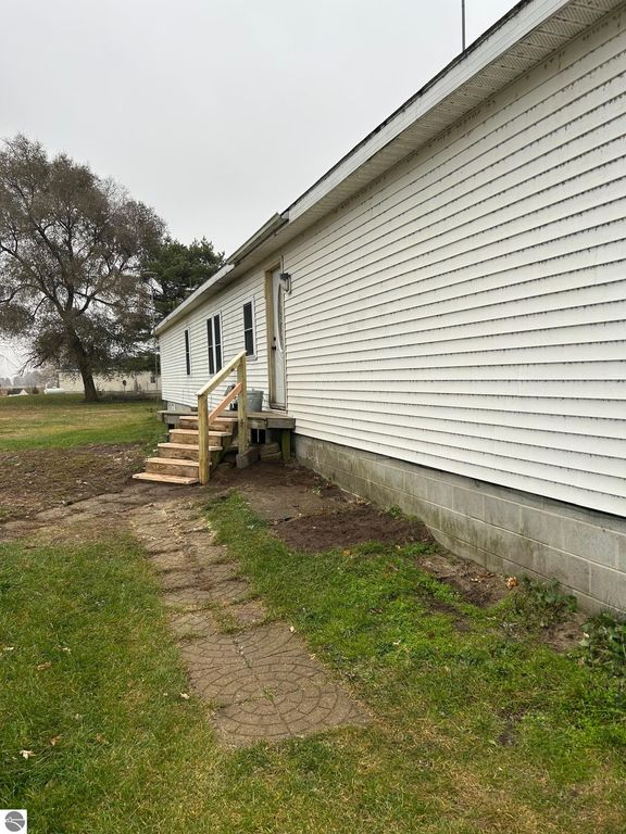Side view of a single-story home at 3780 E North County Line Road, featuring a new wooden front step, white vinyl siding, and a grassy yard, highlighting the property's updated exterior and spacious surroundings.