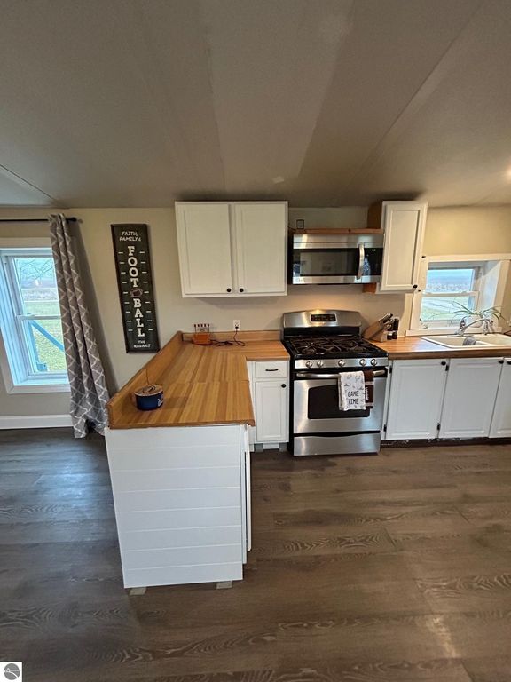 Updated kitchen with white cabinets, stainless steel appliances, and wooden countertop, showcasing a cozy and modern design in a residential property for sale at 3780 E North County Line Road, St Louis, MI.