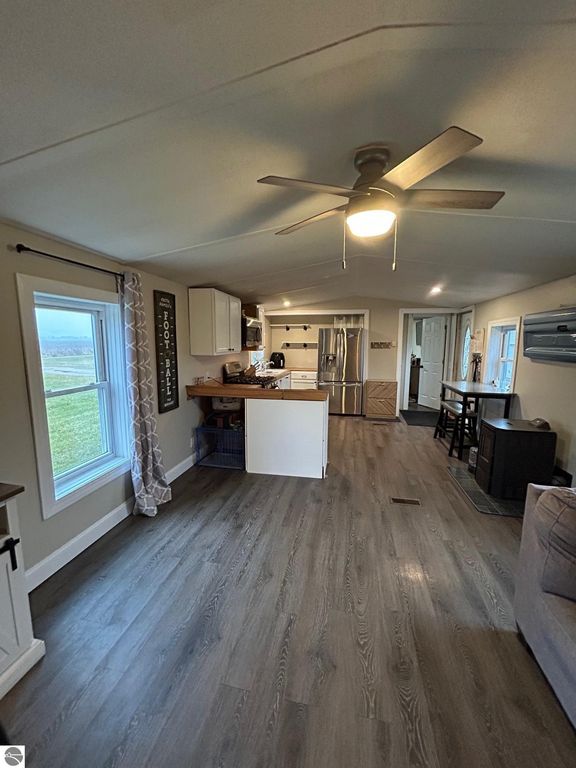 Interior view of updated living space featuring a kitchen with stainless steel appliances, new laminate flooring, ceiling fan, and natural light from windows, highlighting a cozy and modern country home atmosphere.
