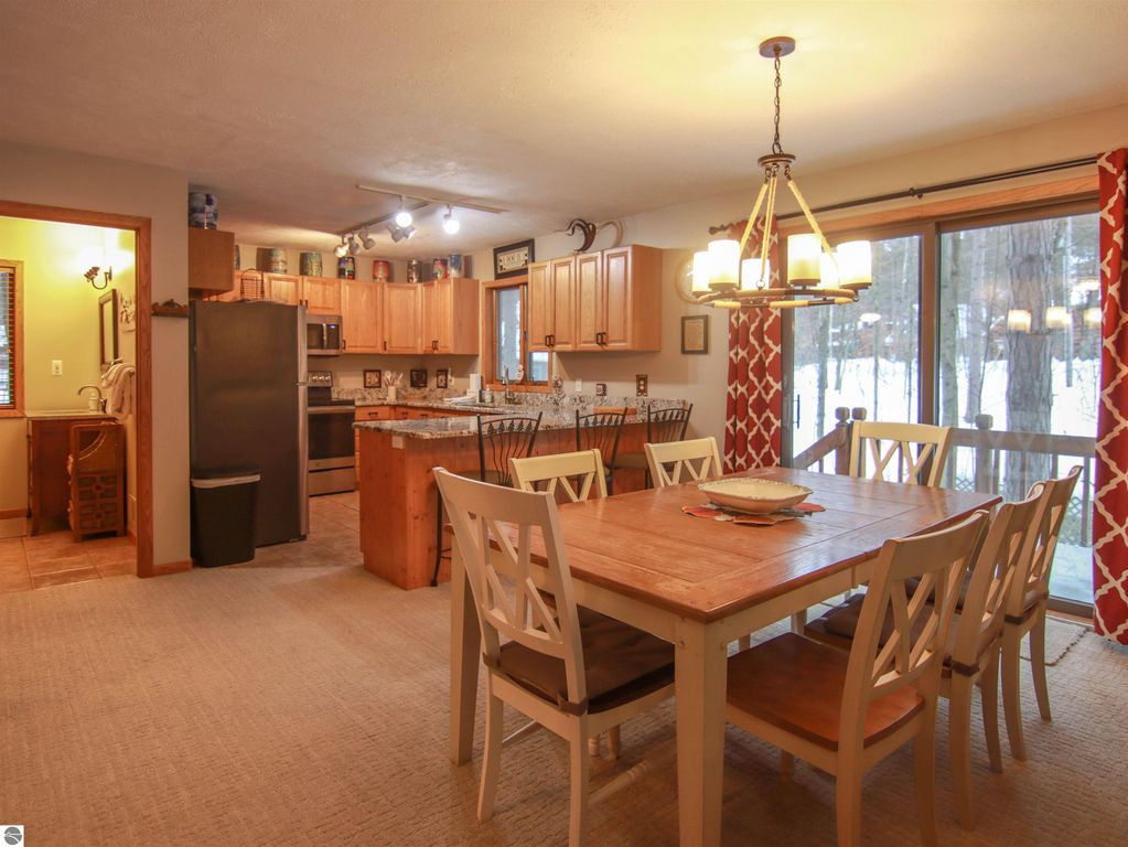 Spacious kitchen and dining area in Crystal Mountain cottage, featuring wooden cabinets, stainless steel appliances, and large dining table with seating, surrounded by tall pines.