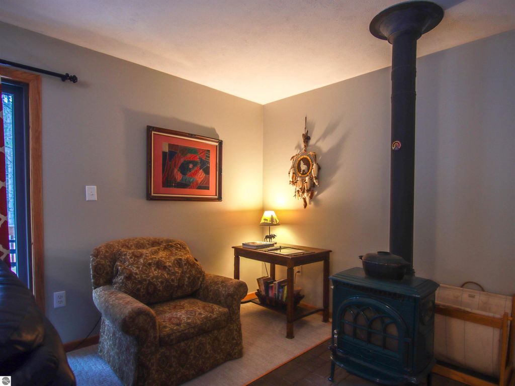 Cozy living area featuring a plush armchair, wooden table with lamp, decorative wall art, and a green wood stove, highlighting the inviting atmosphere of the Crystal Mountain cottage at 7864 Chippewa Drive.