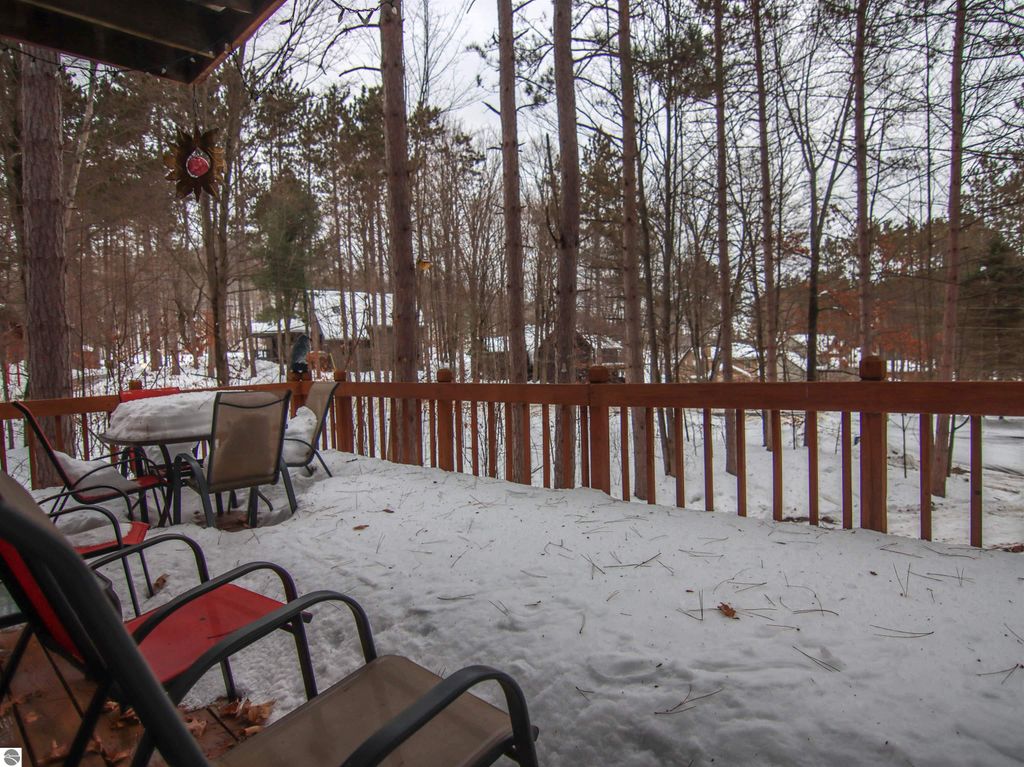 Deck view of snowy landscape surrounded by tall pines near Crystal Mountain cottage, featuring outdoor seating and a peaceful winter setting.