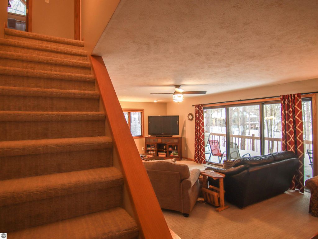 Cozy living room interior of a Crystal Mountain cottage, featuring a ceiling fan, large windows with views of snow-covered trees, a TV, and comfortable seating arrangements, ideal for relaxation after outdoor activities.