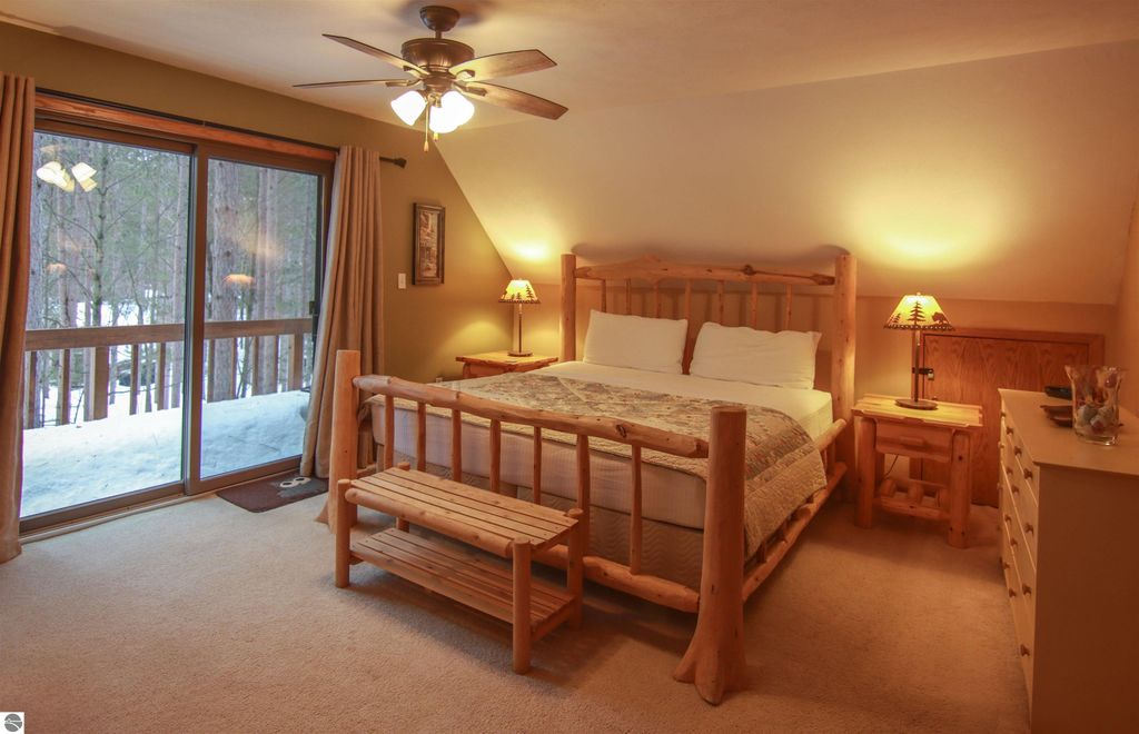 Cozy bedroom in Crystal Mountain cottage featuring log furniture, large windows with forest view, and warm lighting.