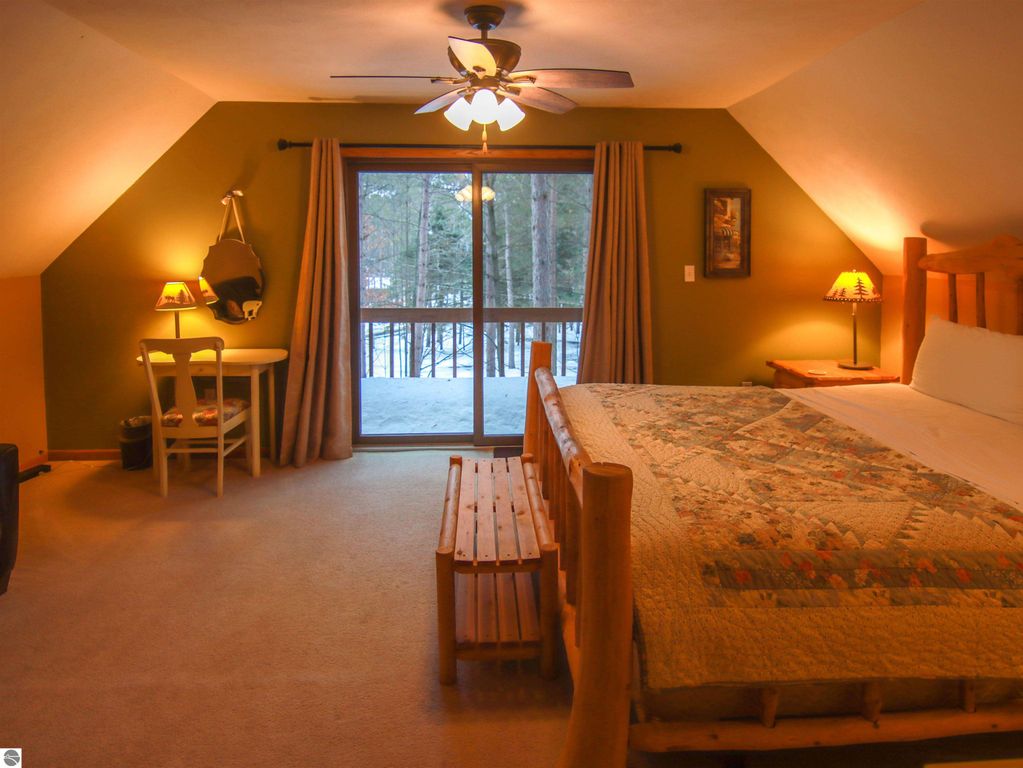 Cozy bedroom in Crystal Mountain cottage featuring a wooden bed, quilted bedding, sitting area with table and chairs, large window with forest view, and warm lighting.