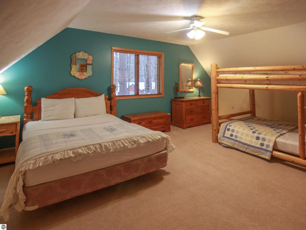 Cozy bedroom with a queen bed and log bunk beds, featuring teal accent wall, wooden furniture, and natural light from window, highlighting the inviting atmosphere of a Crystal Mountain cottage.