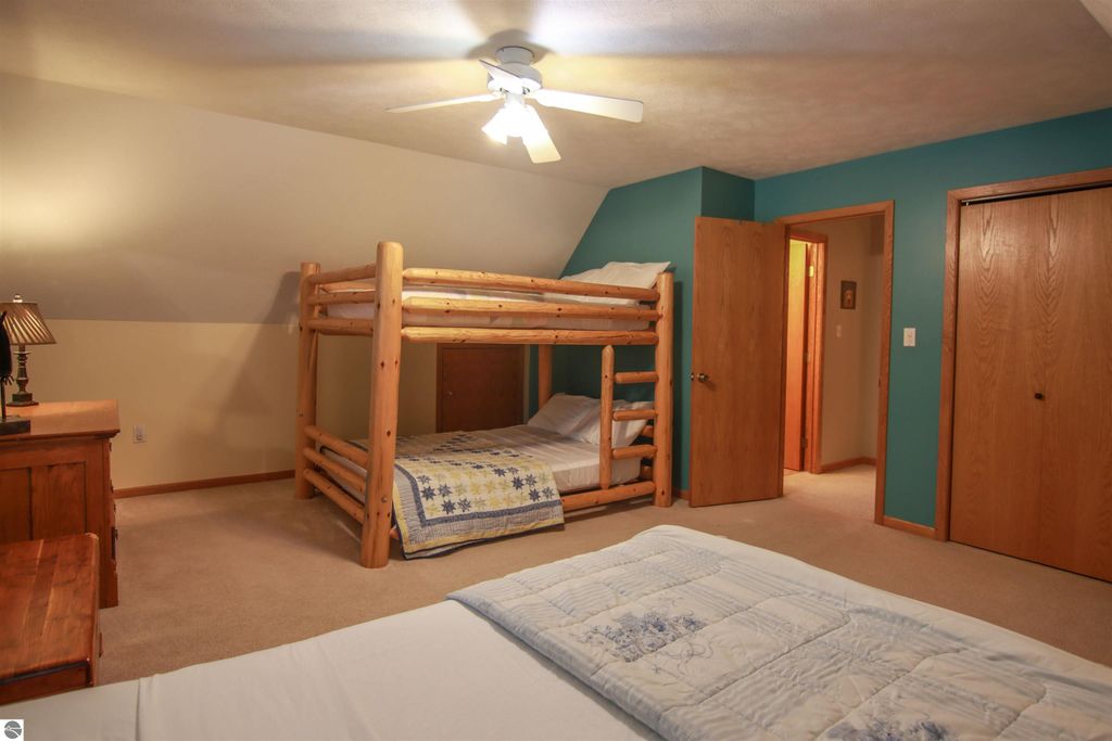 Cozy bedroom with log cabin-style bunk beds, a queen bed, and a warm color palette, highlighting the spacious interior of a Crystal Mountain cottage near ski slopes in Thompsonville, MI.