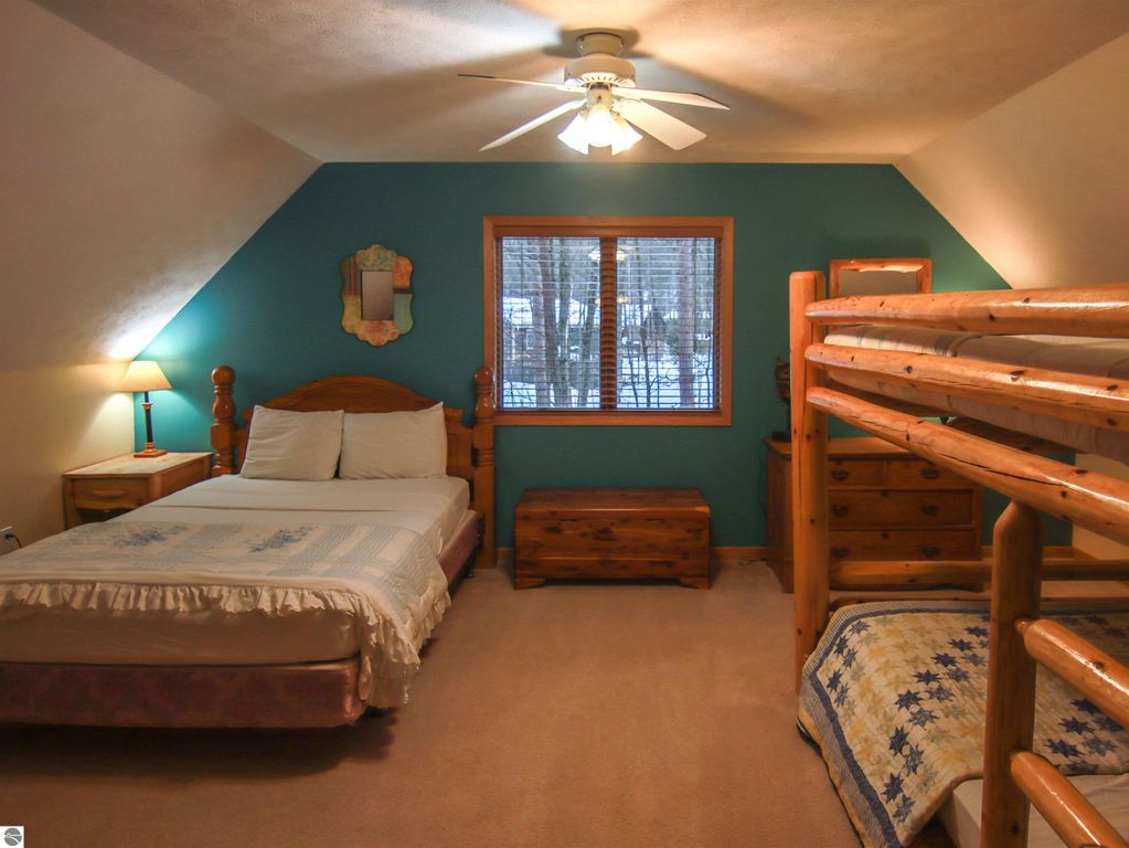 Cozy bedroom featuring a double bed, wooden bunk beds, and a bedside lamp, with a window overlooking tall pines, ideal for a Crystal Mountain cottage experience.