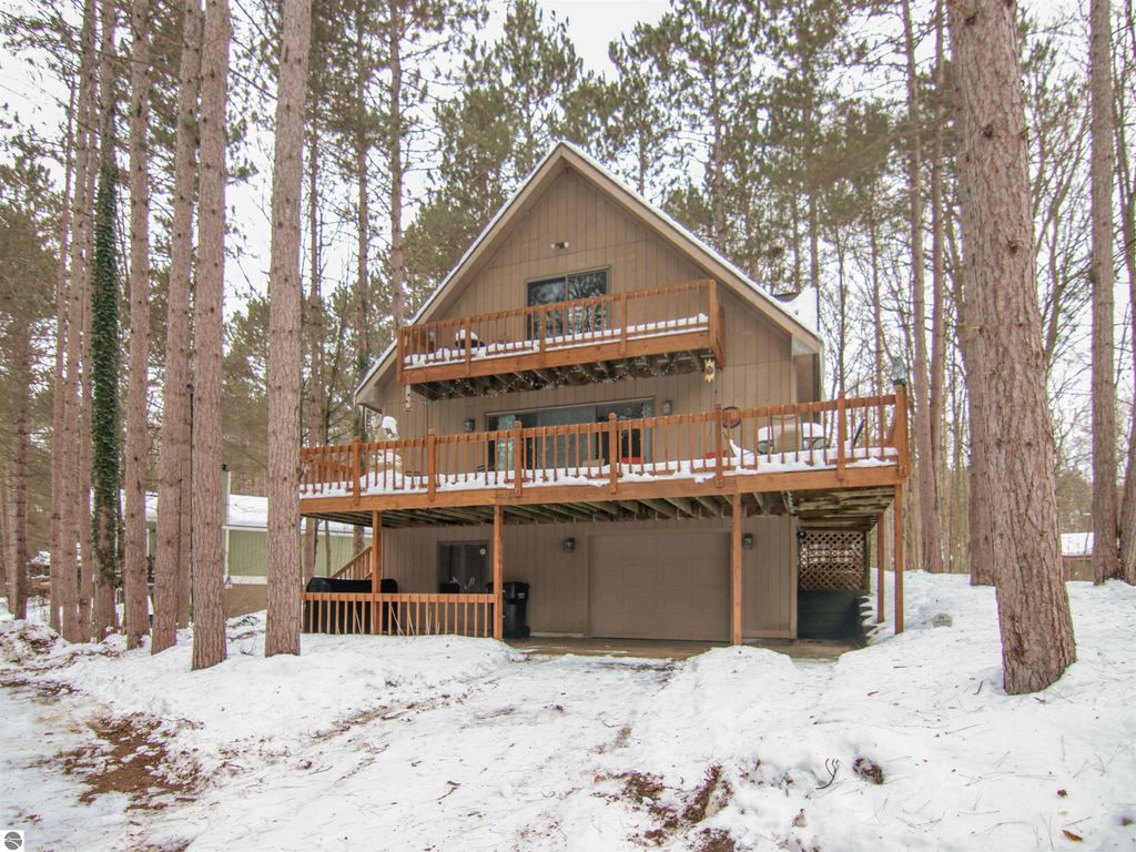 Three-bedroom cottage with wooden deck, nestled among tall pines in snowy Thompsonville, MI, close to ski slopes and amenities.