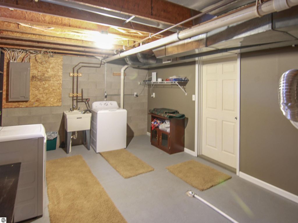 Basement laundry area featuring a washer, utility sink, shelving, and storage cabinet, suitable for a fully furnished 3-bedroom cottage near Crystal Mountain in Thompsonville, MI.
