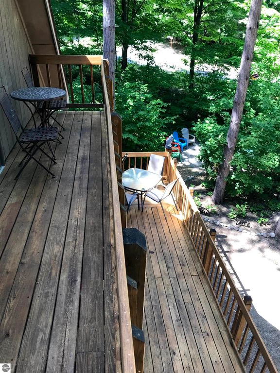 Wooden deck with outdoor seating, surrounded by lush greenery, showcasing a cozy cottage atmosphere near ski slopes in Thompsonville, MI.