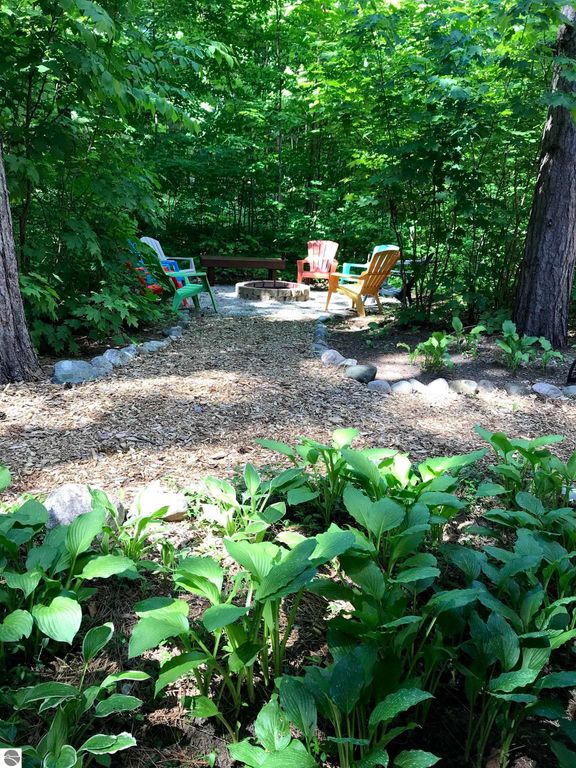 Cozy outdoor seating area with colorful chairs around a fire pit, surrounded by lush greenery and a stone pathway, ideal for relaxing near the Crystal Mountain cottage in Thompsonville, MI.