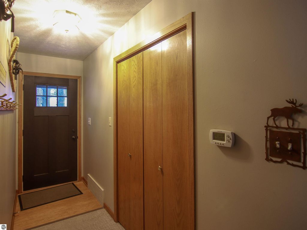 Welcoming entryway of a cottage featuring a dark wooden front door, coat hooks, and storage closet doors, emphasizing the cozy ambiance of the Crystal Mountain property at 7864 Chippewa Drive, Thompsonville, MI.
