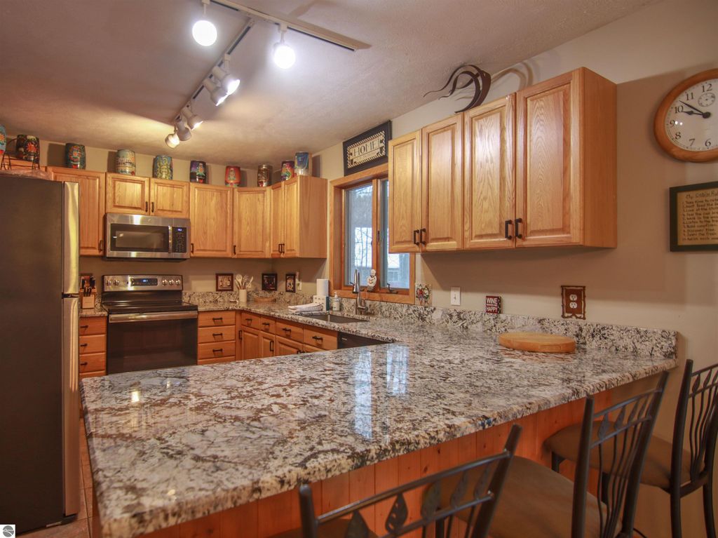 Spacious kitchen with wooden cabinetry, granite countertops, stainless steel appliances, and a cozy dining area, showcasing the inviting interior of a Crystal Mountain cottage in Thompsonville, MI.