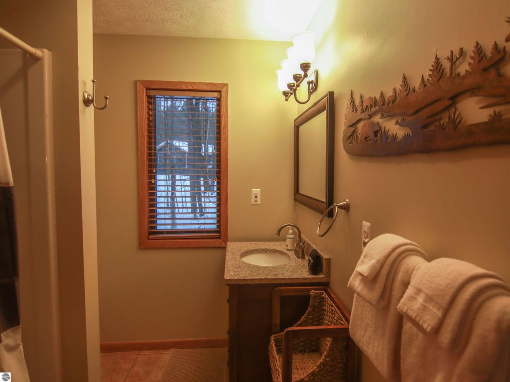 Cozy bathroom in Crystal Mountain cottage featuring a granite countertop sink, wooden accents, plush towels, and a window with blinds overlooking the snowy landscape.
