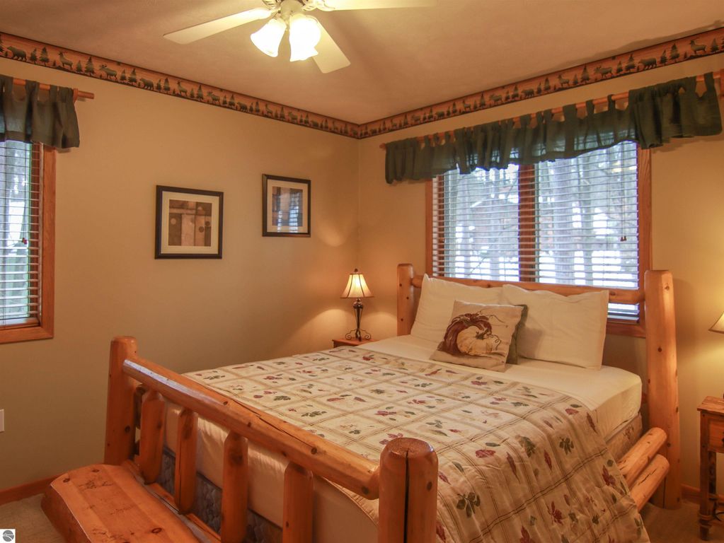 Cozy bedroom in Crystal Mountain cottage featuring a log bed, decorative quilt, and natural light from windows with wooden blinds.