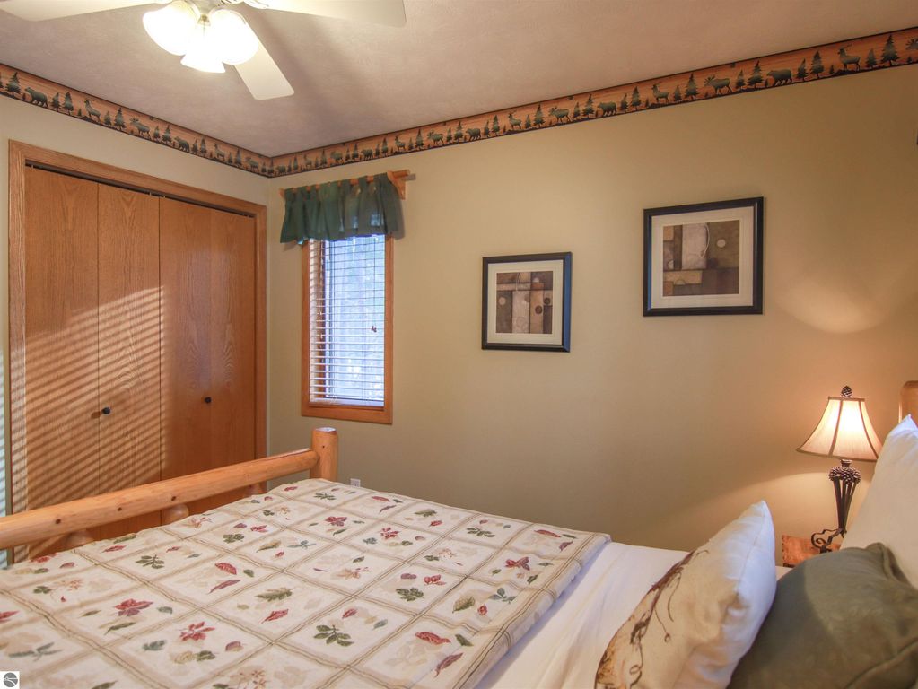 Cozy bedroom in Crystal Mountain cottage featuring a log bed, floral bedding, wooden closet doors, and decorative artwork, with a lamp and window providing natural light.