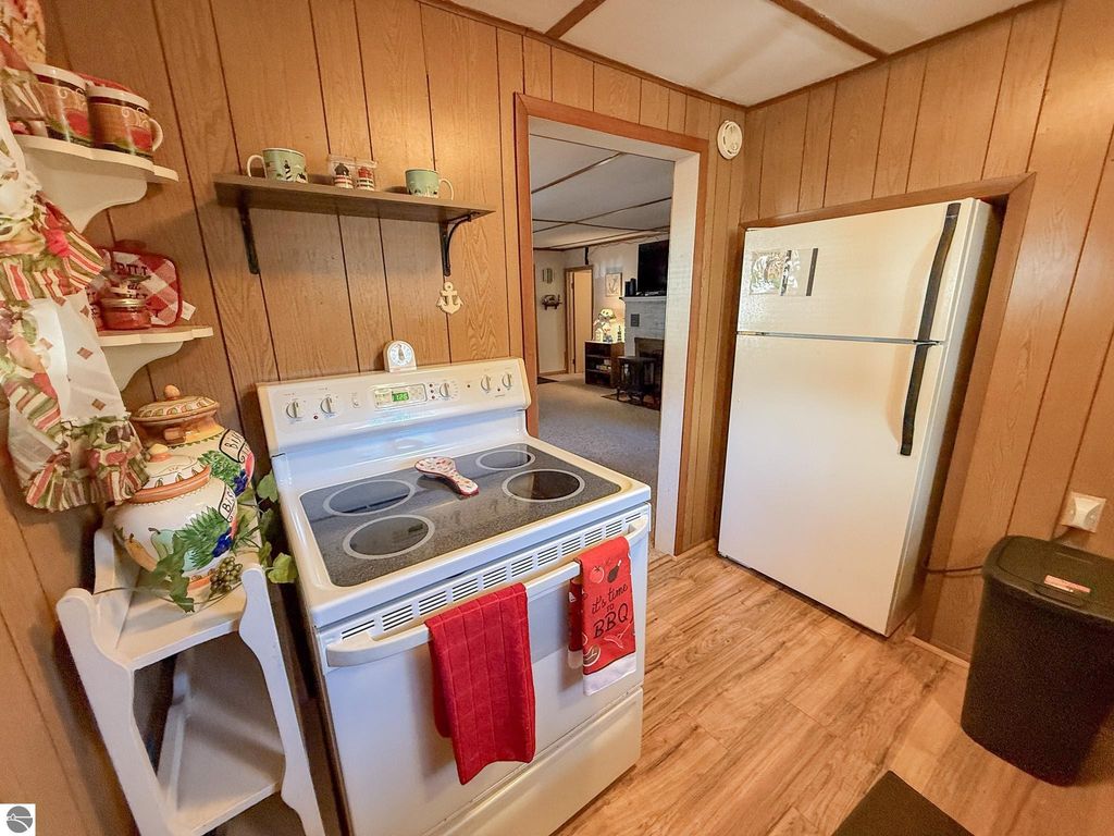 Cozy kitchen interior of a two-bedroom cottage at 133 Maple Bluffs Avenue, featuring a white stove, refrigerator, and wooden walls, decorated with kitchenware and a red BBQ-themed towel.