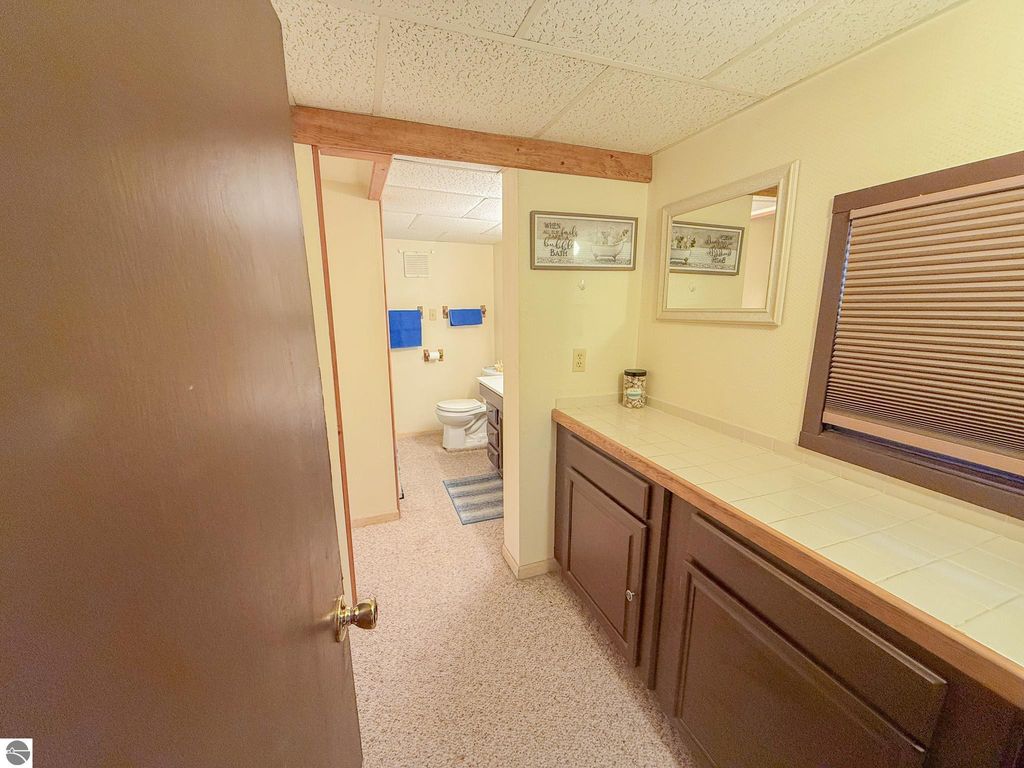 Interior view of a cozy bathroom in a cottage, featuring a toilet, blue towels, and a countertop with storage, emphasizing the homey feel of the property at 133 Maple Bluffs Avenue, Prudenville, MI.