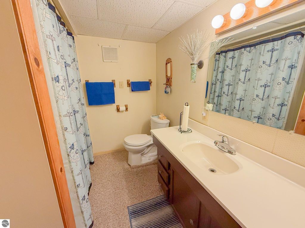 Bathroom with nautical-themed shower curtain, blue towels, sink with faucet, and toilet, showcasing cozy cottage interior at 133 Maple Bluffs Avenue, Prudenville, MI.