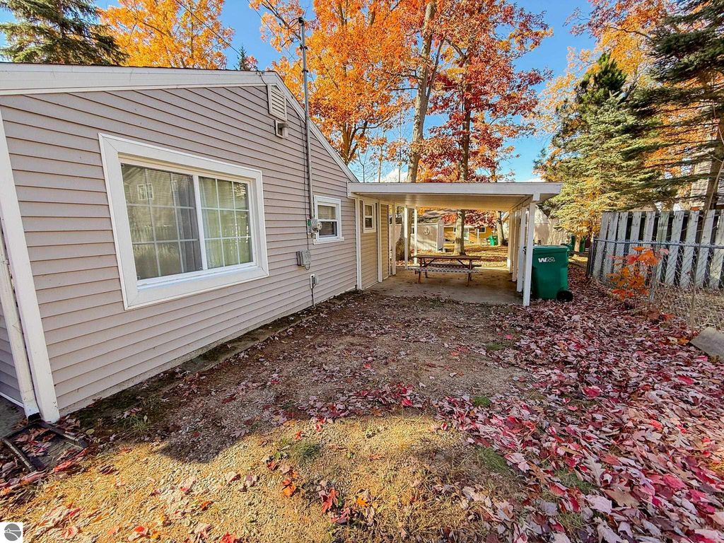 Cottage exterior at 133 Maple Bluffs Avenue, featuring carport and picnic table, surrounded by autumn foliage and fallen leaves, ideal for outdoor gatherings near Houghton Lake.
