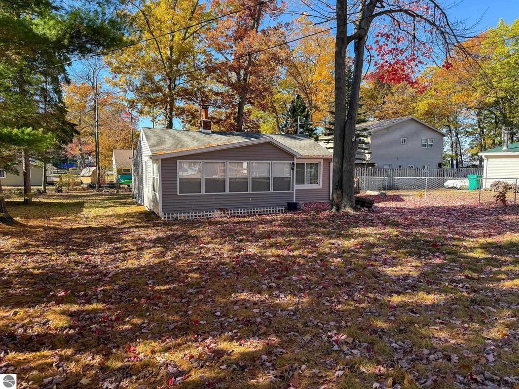 Cottage exterior at 133 Maple Bluffs Avenue, Prudenville, MI, surrounded by autumn foliage and fallen leaves, featuring a cozy design with a screened porch and nearby trees, ideal for an up-north getaway.