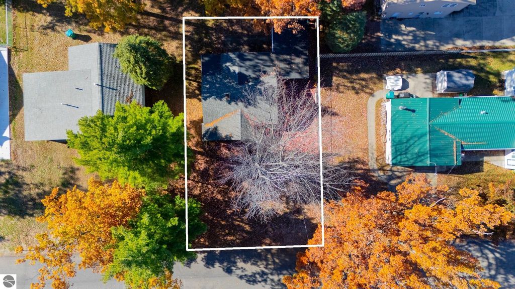 Aerial view of the cottage at 133 Maple Bluffs Avenue in Prudenville, MI, surrounded by autumn foliage, showcasing nearby homes and outdoor space.