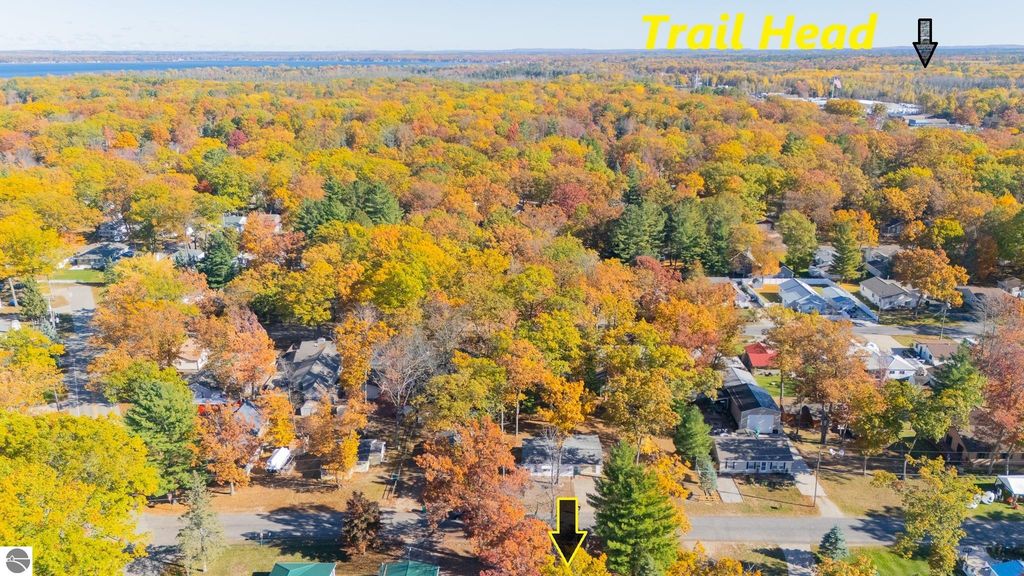Aerial view of colorful autumn foliage surrounding Prudenville, MI, highlighting nearby trailhead access and residential areas, ideal for outdoor enthusiasts.