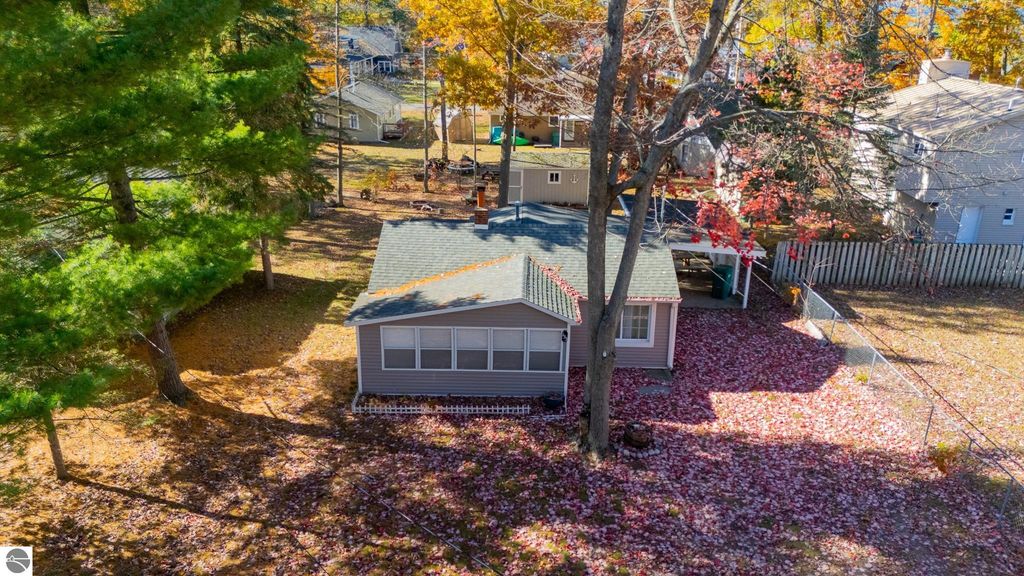 Aerial view of a cozy two-bedroom cottage at 133 Maple Bluffs Avenue, Prudenville, MI, surrounded by autumn foliage, featuring a carport, backyard shed, and spacious yard.