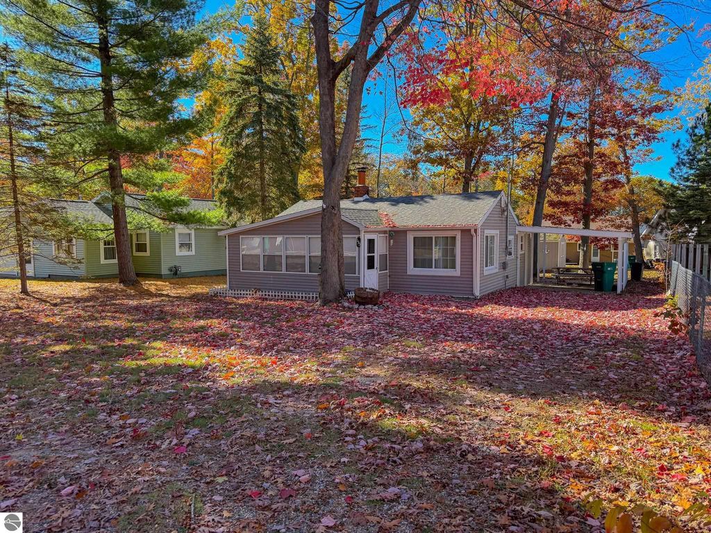 Cottage at 133 Maple Bluffs Avenue in Prudenville, MI, surrounded by autumn foliage, featuring a cozy carport and backyard shed, ideal for outdoor living and storage.