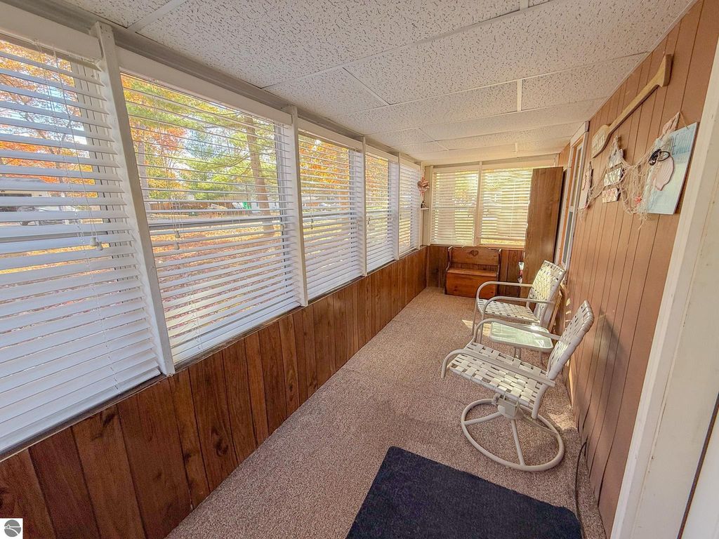 Cozy sunroom with two white rocking chairs, wooden paneling, and large windows showcasing autumn foliage outside, ideal for relaxing in a cottage at 133 Maple Bluffs Avenue, Prudenville, MI.