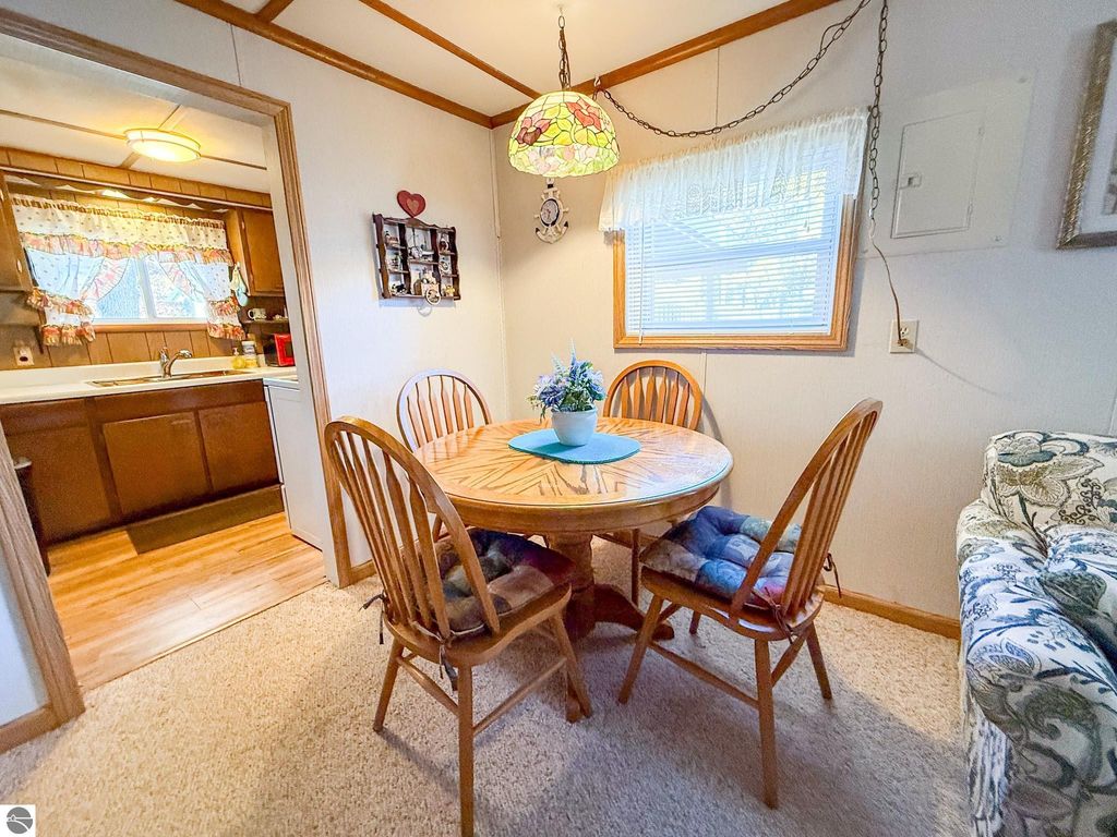 Cozy dining area featuring a round wooden table with four chairs, colorful pendant light, and a view of the kitchen in a two-bedroom cottage at 133 Maple Bluffs Avenue, Prudenville, MI.