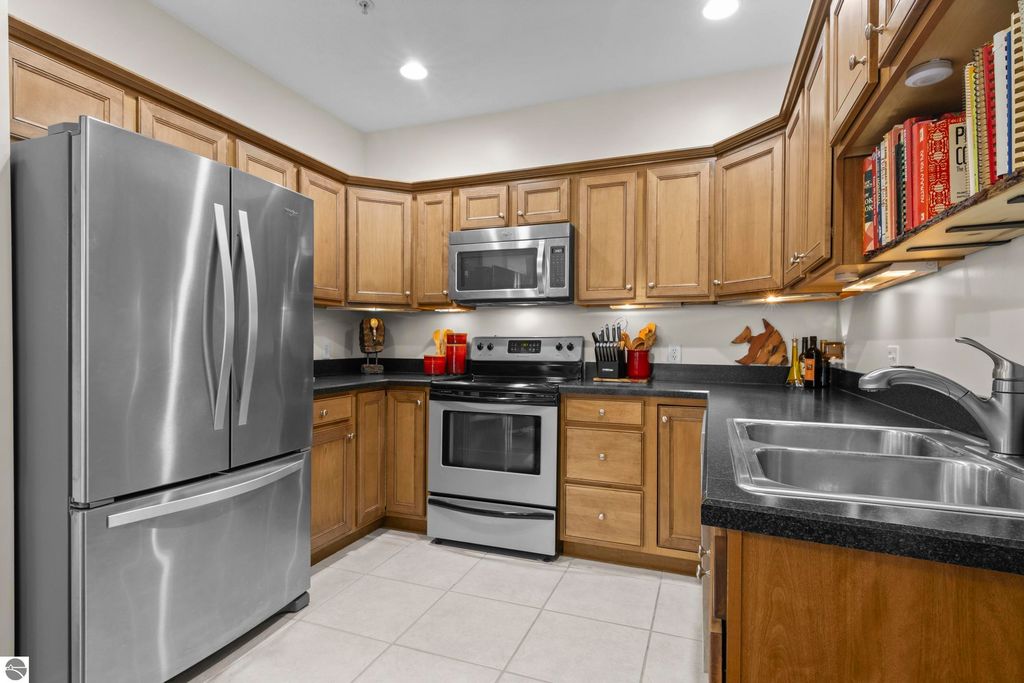 Modern kitchen featuring stainless steel appliances, wooden cabinetry, black countertops, and a double sink, showcasing the well-maintained interior of the 2-bedroom condo in Traverse City.