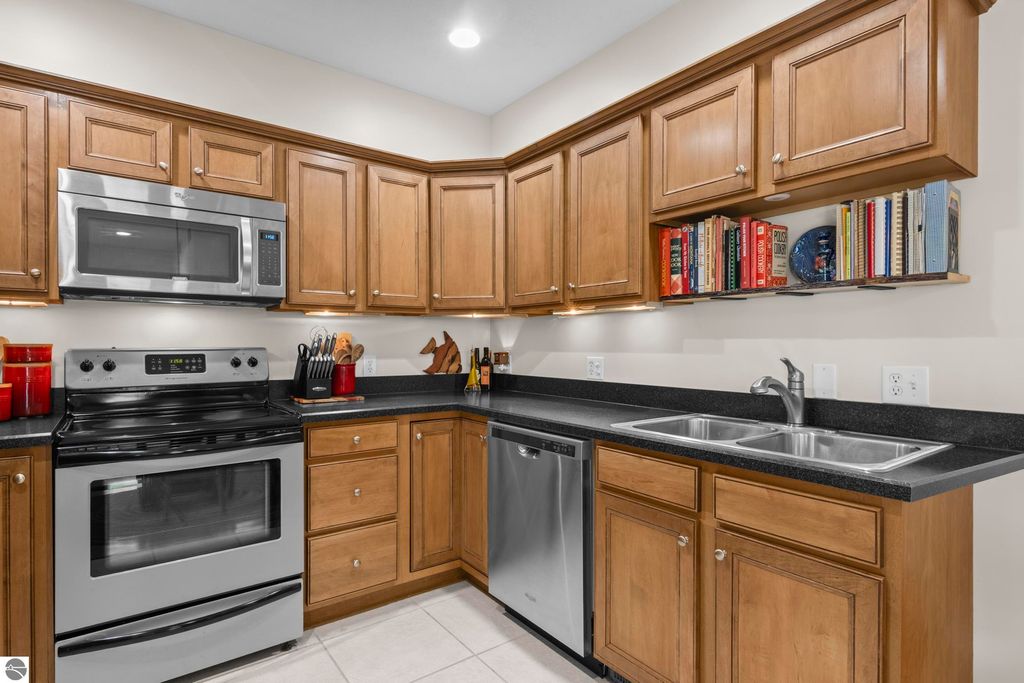 Modern kitchen with stainless steel appliances, wood cabinetry, and black countertops, featuring a gas stove, microwave, and double sink, ideal for the 2-bedroom condo in Traverse City.