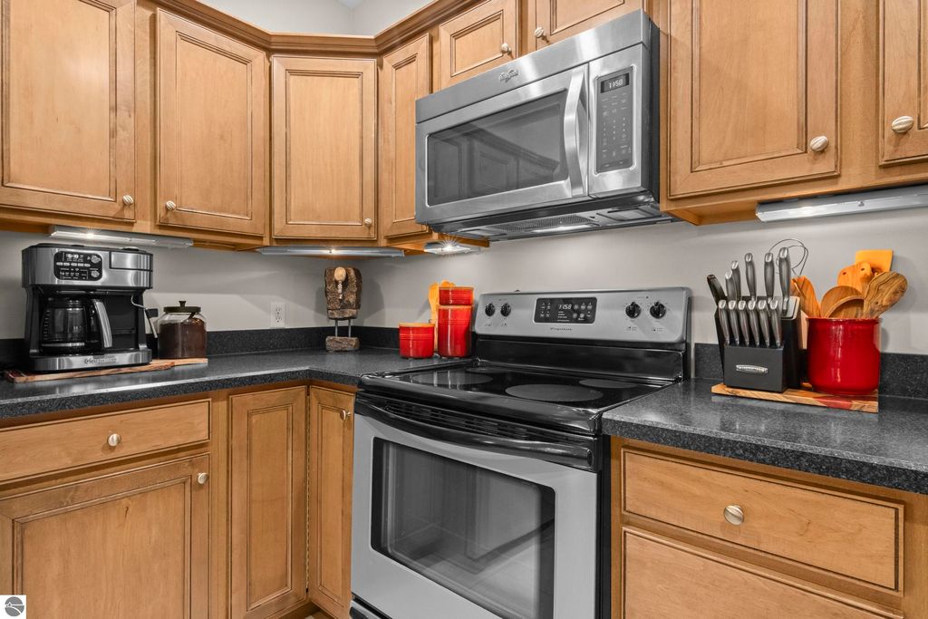 Modern kitchen with stainless steel appliances, including a microwave and stove, surrounded by wooden cabinetry, featuring a coffee maker and utensils, highlighting the condo's inviting interior in Traverse City, MI.