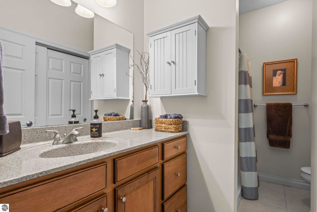 Bathroom interior featuring a granite countertop with dual sinks, wooden cabinetry, decorative wall cabinet, and neutral-colored walls, highlighting a clean and modern design in a 2-bedroom condo in Traverse City.