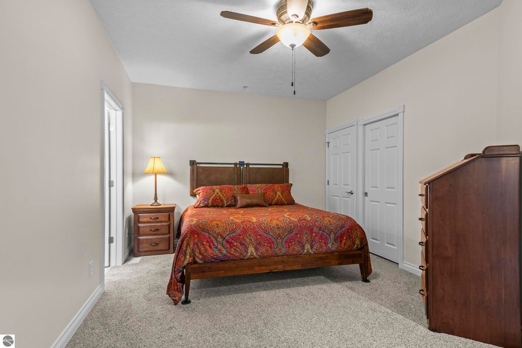 Cozy bedroom featuring a wooden bed with colorful bedding, bedside lamp, and dresser, showcasing a clean and inviting living space in a 2-bedroom condo in Traverse City, MI.