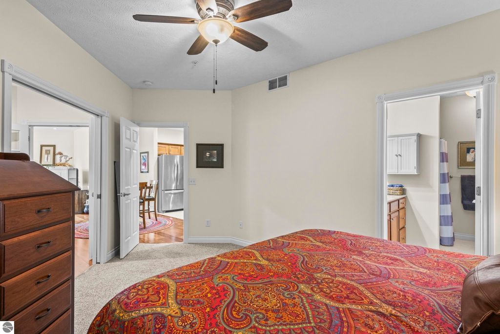 Bedroom interior of a 2-bedroom condo in Traverse City, featuring a colorful patterned bedspread, ceiling fan, and doorways leading to adjacent rooms, showcasing an open floor plan and inviting atmosphere.