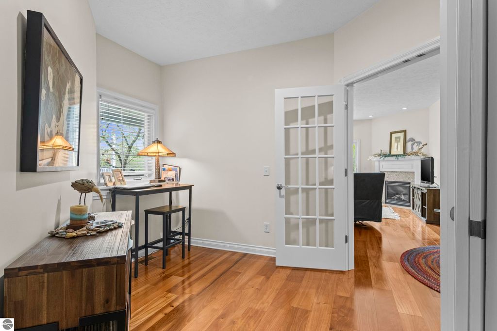 Cozy interior of a 2-bedroom condo in Traverse City, featuring a home office nook with a desk and lamp, hardwood floors, and a view into a living area with a gas fireplace.