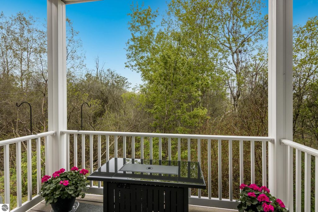 Balcony view with a black table and pink flowers, surrounded by lush greenery, showcasing peaceful outdoor living space near Traverse City condo.