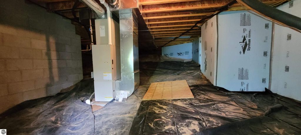 Crawl space of a condominium featuring insulated walls, a furnace, and a clean, dry floor, showcasing ample storage potential in the Traverse City property listing.