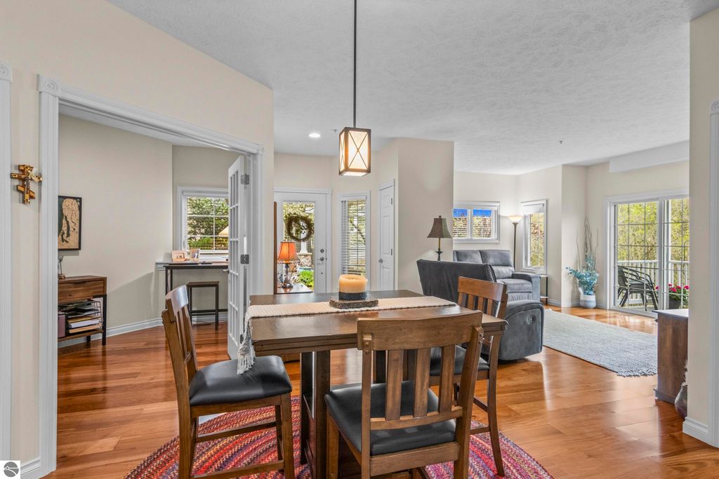 Interior view of a cozy 2-bedroom, 2-bath condo in Traverse City, featuring a dining table, hardwood floors, and an open layout with natural light, showcasing a comfortable living area and access to a private balcony.