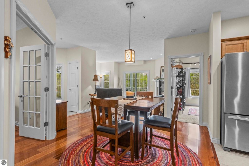 Cozy dining area featuring a wooden table and chairs, with a view of the living space and natural light from large windows, in a well-maintained 2-bedroom condo in Traverse City, MI.