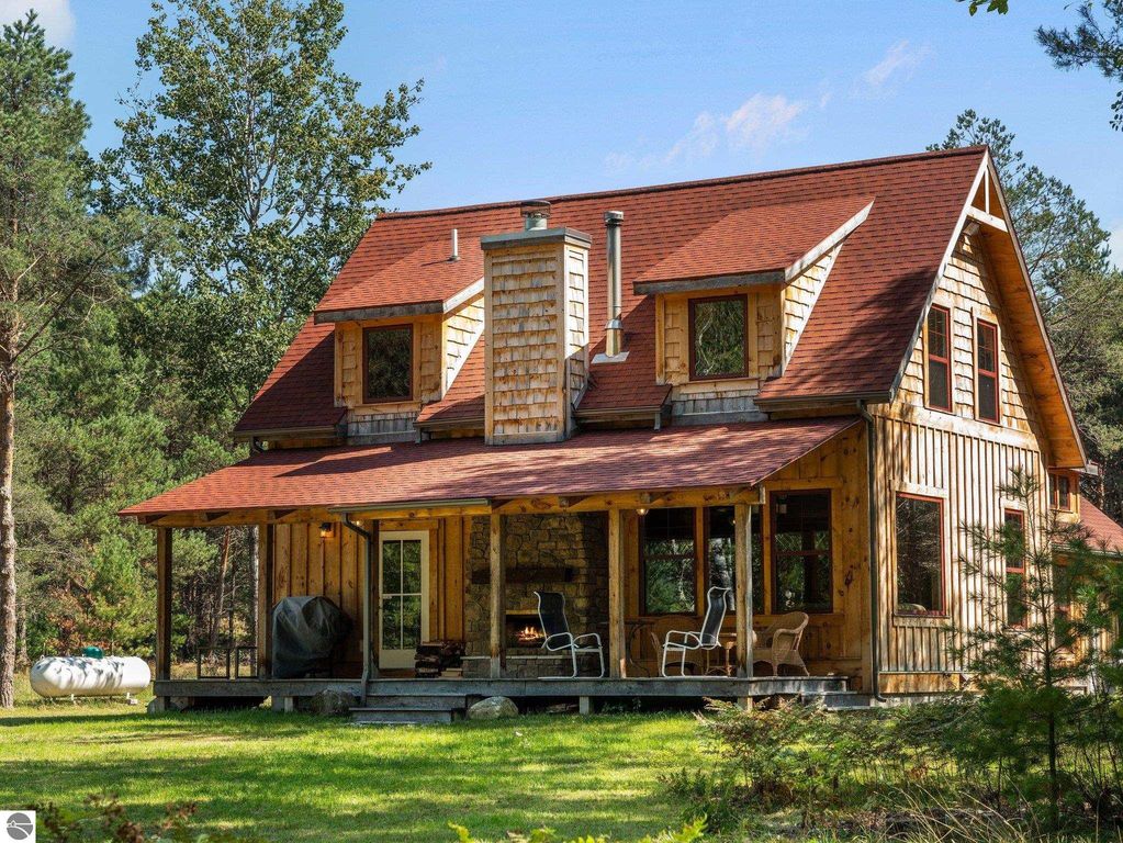 Custom-built wooden home in northern Michigan, featuring a rustic design, large front porch, and surrounded by lush greenery on 10 acres, ideal for outdoor living and relaxation.