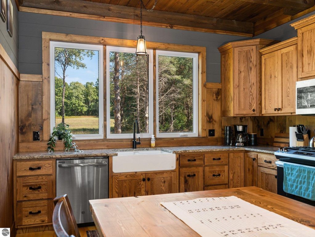 Custom-built kitchen with wooden cabinets, granite countertops, large windows showcasing northern Michigan countryside views, and modern appliances.